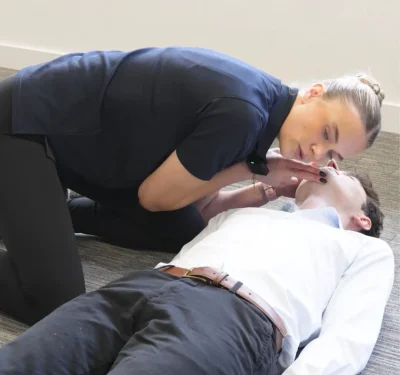 Demonstrating epilepsy first aid by checking on a person lying on the floor during a seizure response scenario.