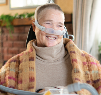 A smiling adult client with a tracheostomy tube, interacting confidently with trained care staff while managing complex needs.