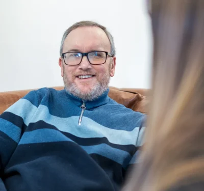 Komplex Care neurological care client smiling and having a conversation while sitting comfortably at home.
