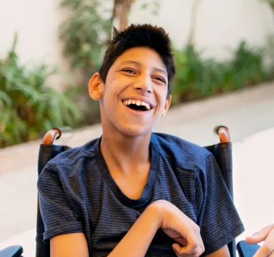 Komplex Care client with cerebral palsy smiling while sitting in a wheelchair, enjoying a happy moment.